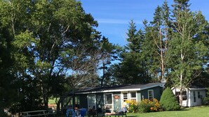 A lodge with a covered porch, picnic tables, and a lawn. - River Meadow Camp Cottage (Summerside)