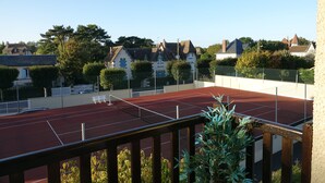 A tennis court with a wooden railing, surrounded by residential houses and greenery. - Pleasant pied-à-terre on the Côte Fleurie Rated 3 stars by Gîtes de France (Cabourg)