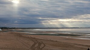A beach with a wide sandy area, a few people, and a cloudy sky with sunlight breaking through. - Pleasant pied-à-terre on the Côte Fleurie Rated 3 stars by Gîtes de France (Cabourg)