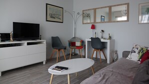 A modern living room with a flat-screen TV, white entertainment unit, two chairs, a small round table, and a sofa. - Pleasant pied-à-terre on the Côte Fleurie Rated 3 stars by Gîtes de France (Cabourg)