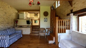 A rustic interior with a wooden staircase, a sofa, a chair, and a kitchen area.