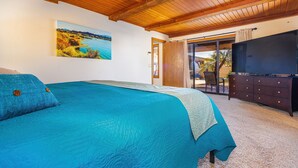 Ein Schlafzimmer mit einem großen Bett, einem Deckenventilator, einem Gemälde, einem Fernseher und einer Glasschiebetür, die auf einen Balkon führt.