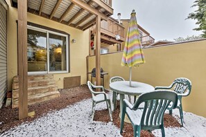 En terrasse med bord og stole, en stribet parasol og et træterrasse.