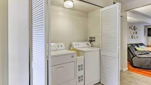 Ein Waschraum mit zwei weißen Waschmaschinen und Trocknern, einer Deckenleuchte und einer Schiebetür zu einem Kleiderschrank.