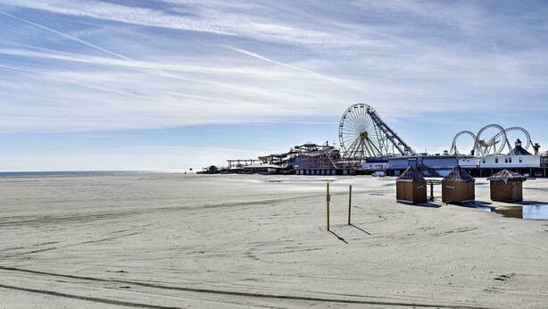 Ein Strand mit einem großen Riesenrad und einer Promenade mit kleinen Holzhäusern.