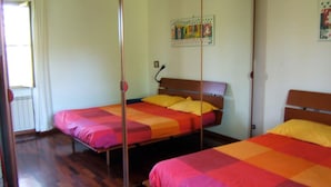 Quarto com duas camas, cada uma com colcha colorida. Há um espelho em uma parede e um cartaz sobre as camas.