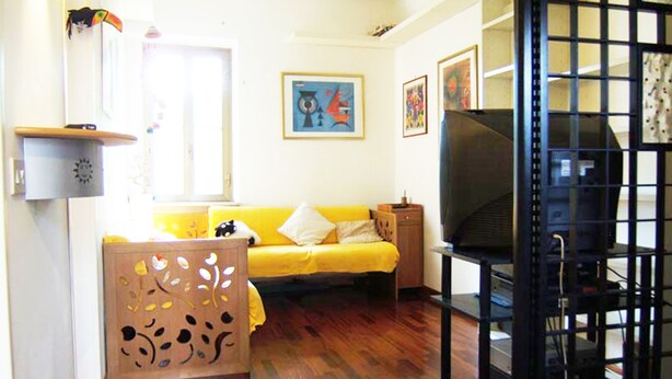 Uma sala de estar com um sofá amarelo, uma televisão e obras de arte na parede.