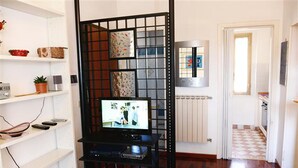 Quarto com televisão sobre um suporte preto, radiador branco e chão quadriculado.