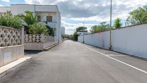 Una calle residencial tranquila con edificios blancos, cielo despejado y un farol.