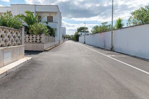Una calle residencial tranquila con edificios blancos, cielo despejado y un farol.