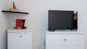 Una kitchenette con cafetera, un televisor sobre un tocador y un cactus en una repisa.