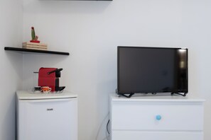 Una kitchenette con cafetera, un televisor sobre un tocador y un cactus en una repisa.