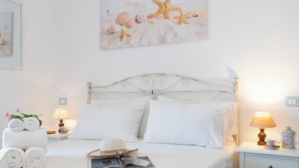 Una cama bien tendida con sábanas blancas, un cabecero decorativo y una mesita de noche con una lámpara y un objeto decorativo.