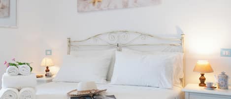 A neatly made bed with white linens, a decorative headboard, and a bedside table with a lamp and a decorative item.
