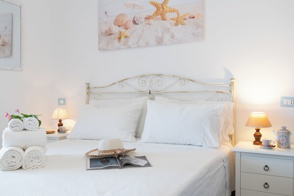 A neatly made bed with white linens, a decorative headboard, and a bedside table with a lamp and a decorative item.