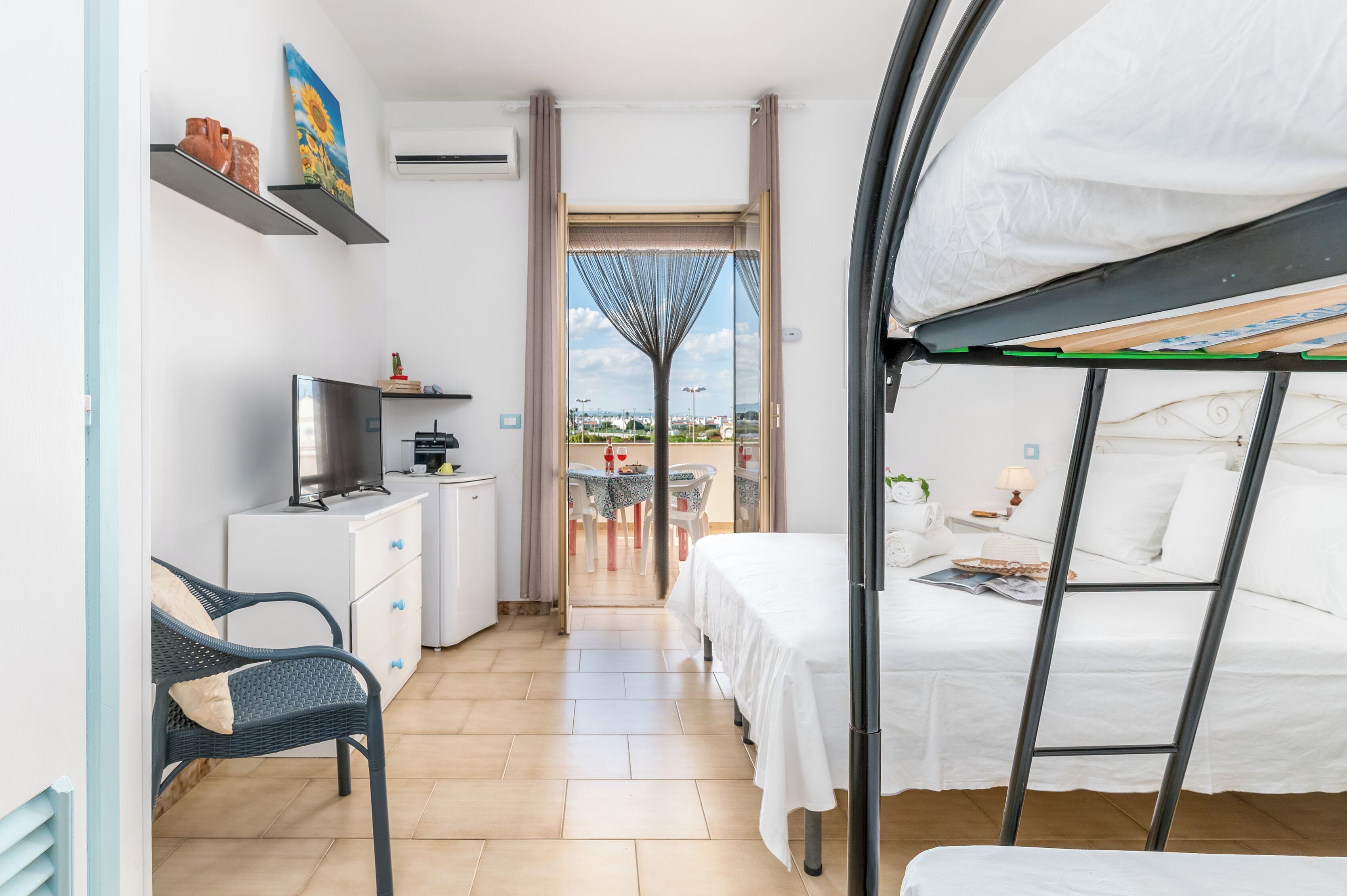 A compact hotel room with a bed, a desk, a chair, and a view through a door.