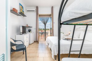 Habitación de hotel pequeña con una cama, un escritorio, una silla y vistas a través de una puerta.