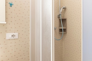 A shower with a handheld hose, a wall-mounted electrical outlet, and patterned tiles.
