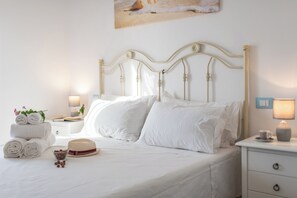 A neatly made bed with white linens, a decorative hat, and rolled towels on the side. - Monolocale vista giardino-Studio-Balcony-Private Bathroom (Ostuni)