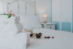 Cama bem arrumada com toalhas dobradas e um recipiente com castanhas, uma luminária de cabeceira e uma mesinha de apoio.