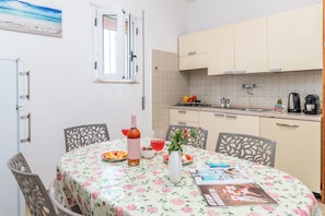 A dining area with a table set for two, a kitchen with beige cabinets, and a window with blinds.