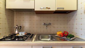 Una cocina con estufa a gas, lavamanos y un frutero con verduras.