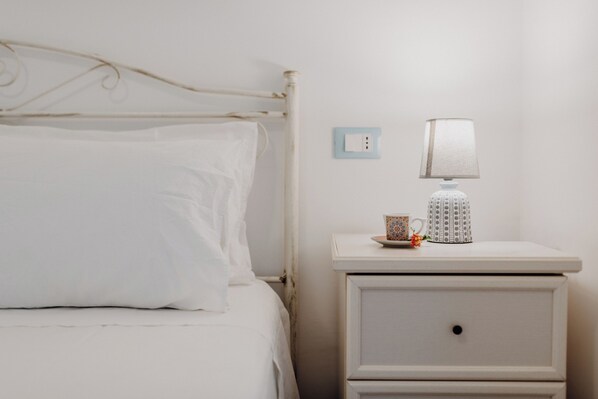 Una cama con ropa blanca, una mesita de noche con una lámpara y una taza.
