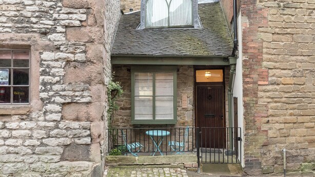 A narrow street with a stone building featuring a large window and a door with a number plate. - 1 bedroom accommodation in Wirksworth, near Matlock (Wirksworth, near Matlock)