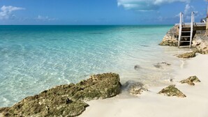 A beach with clear turquoise water, rocky outcrops, and a ladder leading to a structure on the right.