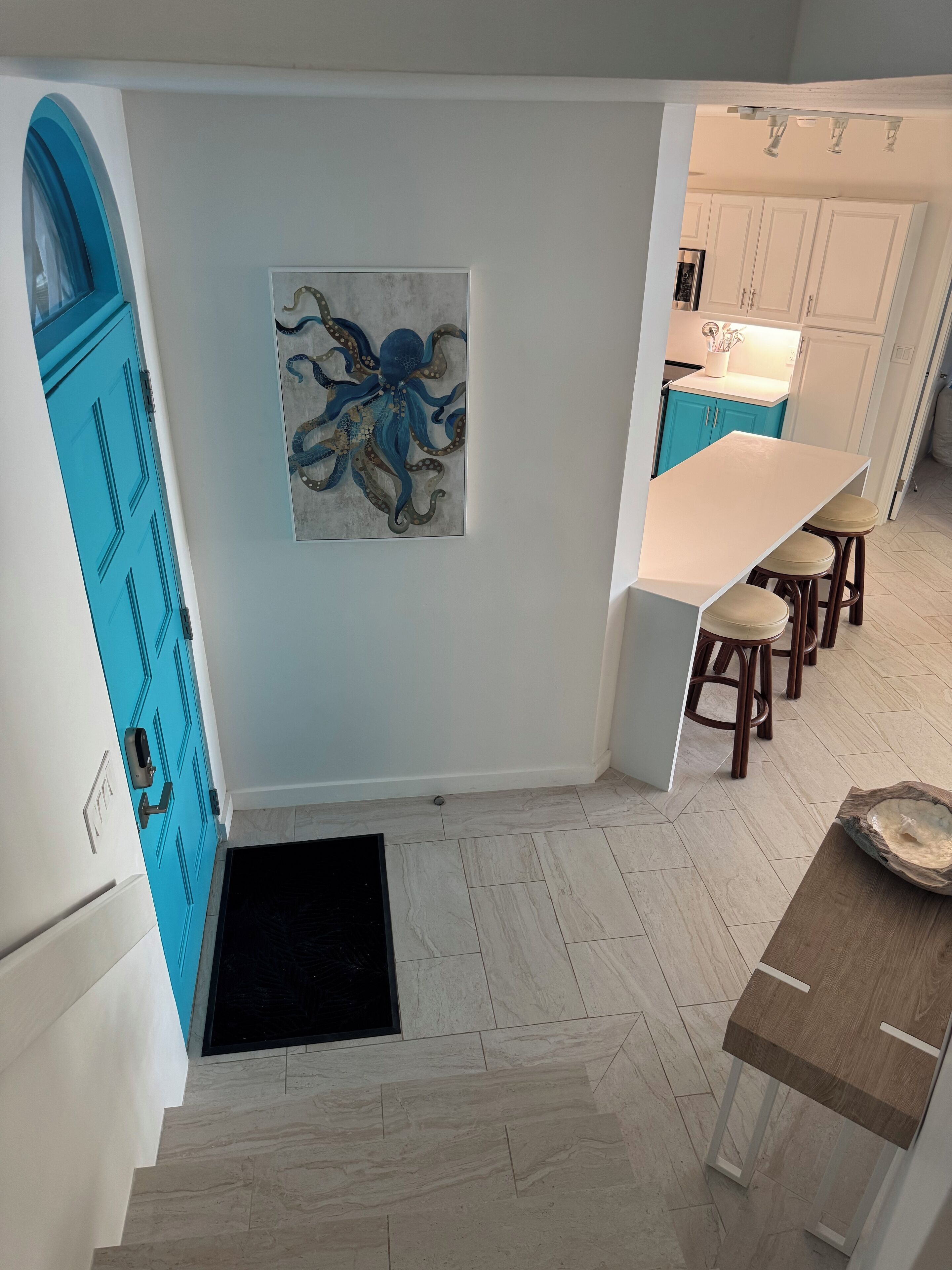 A modern kitchen with a white countertop, blue cabinets, and a large octopus painting on the wall.