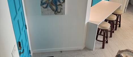A modern kitchen with a white countertop, blue cabinets, and a large octopus painting on the wall.