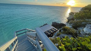 A wooden staircase leading to a deck overlooking a turquoise sea with a sunset in the background.