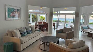 A spacious living area with a sofa, chairs, and a coffee table. There is a dining table with chairs and a view of the ocean through large windows.