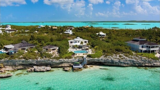 An aerial view of a coastal property with multiple houses, a swimming pool, and clear turquoise waters.