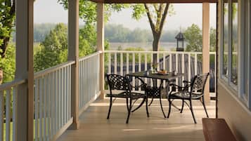 A covered outdoor area with a table and chairs, overlooking a body of water and trees.