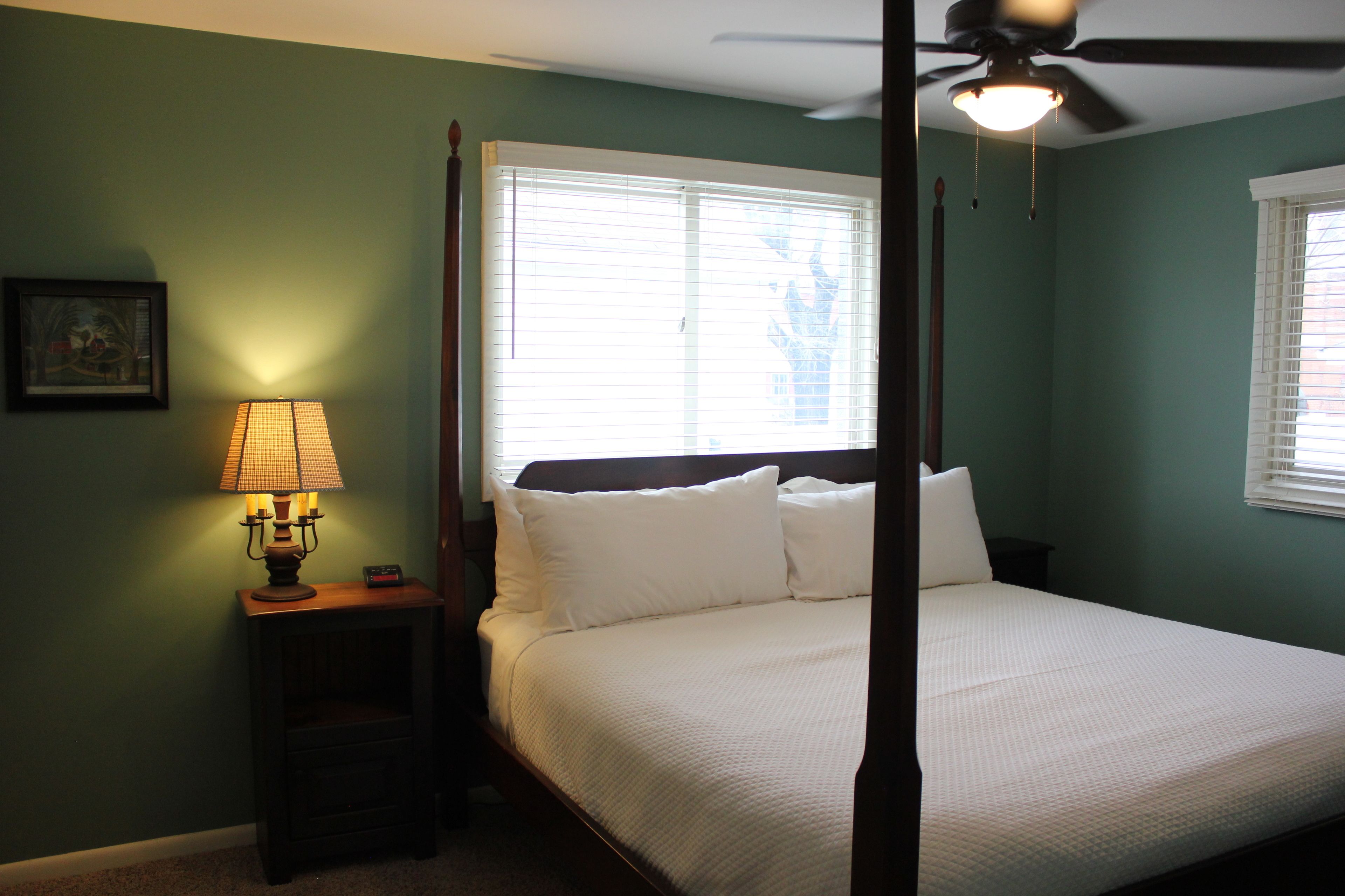 A bedroom with a four-poster bed, a standing lamp, and a ceiling fan.