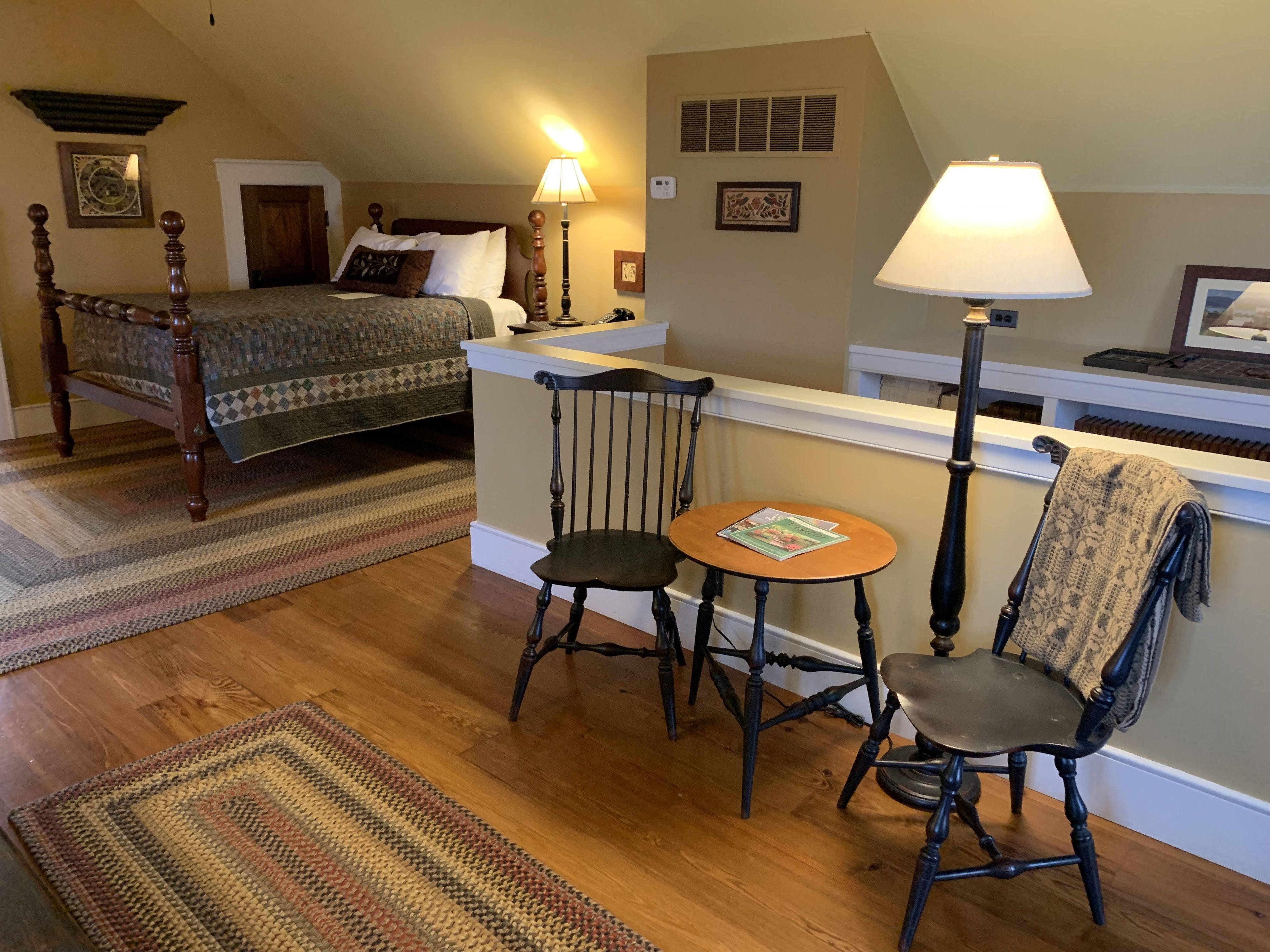 A cozy room with a bed, a small table, two chairs, a lamp, and a radiator.