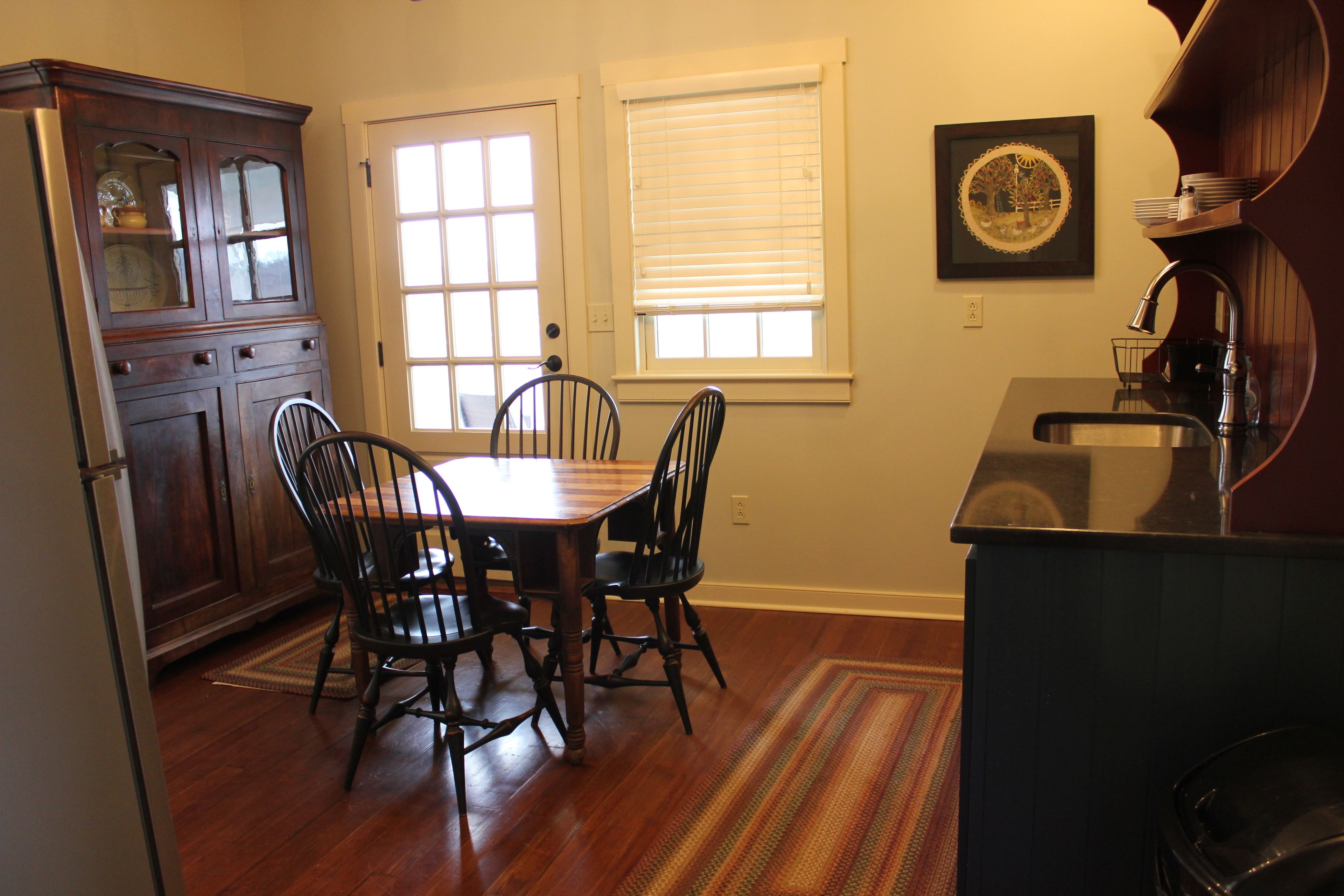 A dining area with a wooden table and chairs, a kitchen with a sink and cabinets, and a window with blinds.
