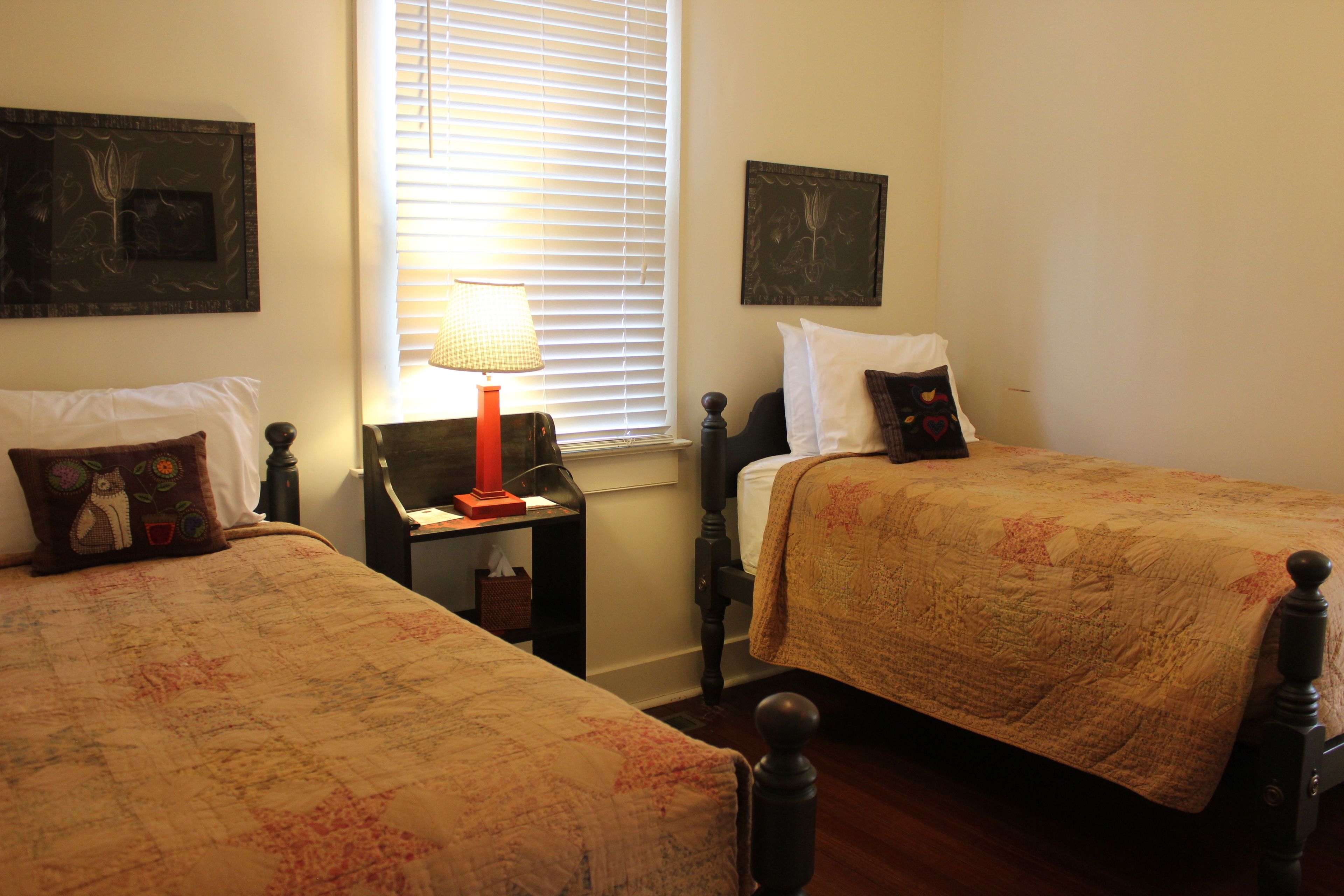 A bedroom with two single beds, a nightstand with a lamp, and a window with blinds.