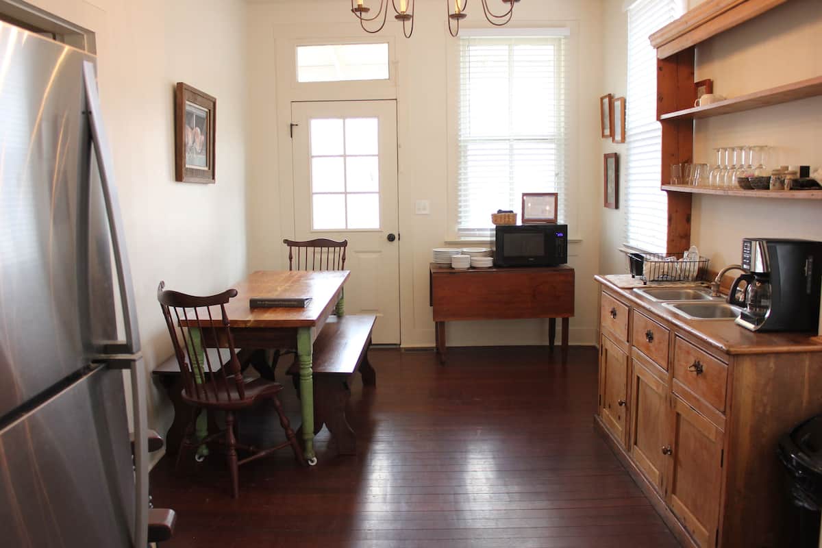 A kitchen with wooden cabinets, a refrigerator, a dining table with chairs, and a window with blinds.