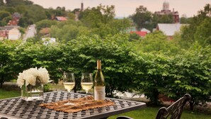 A table with a bottle of wine, two glasses, and a vase of flowers. - Inn at Hermannhof (Hermann)
