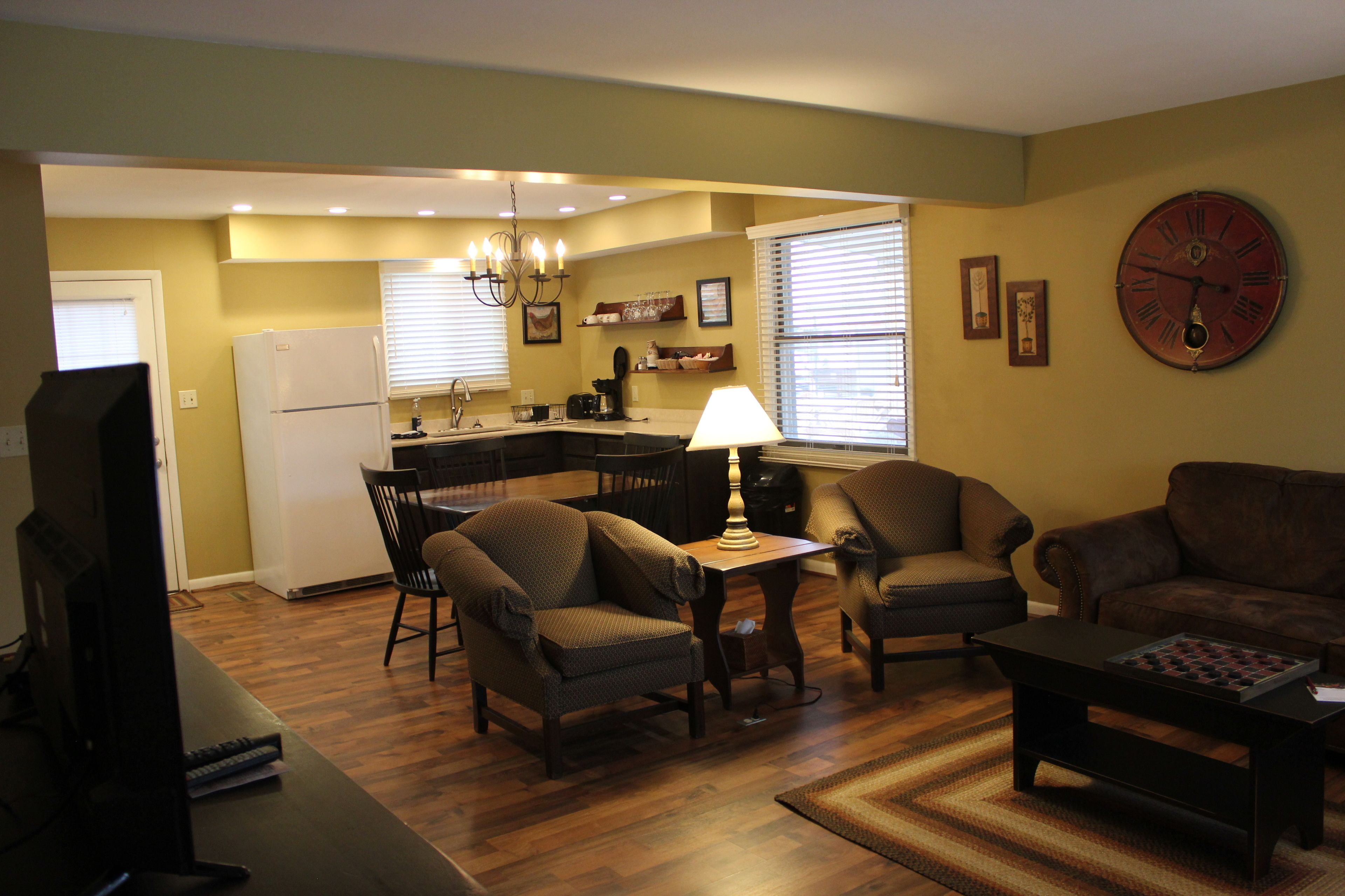 A living room with a TV, two sofas, a coffee table, and a dining area with a kitchen in the background.