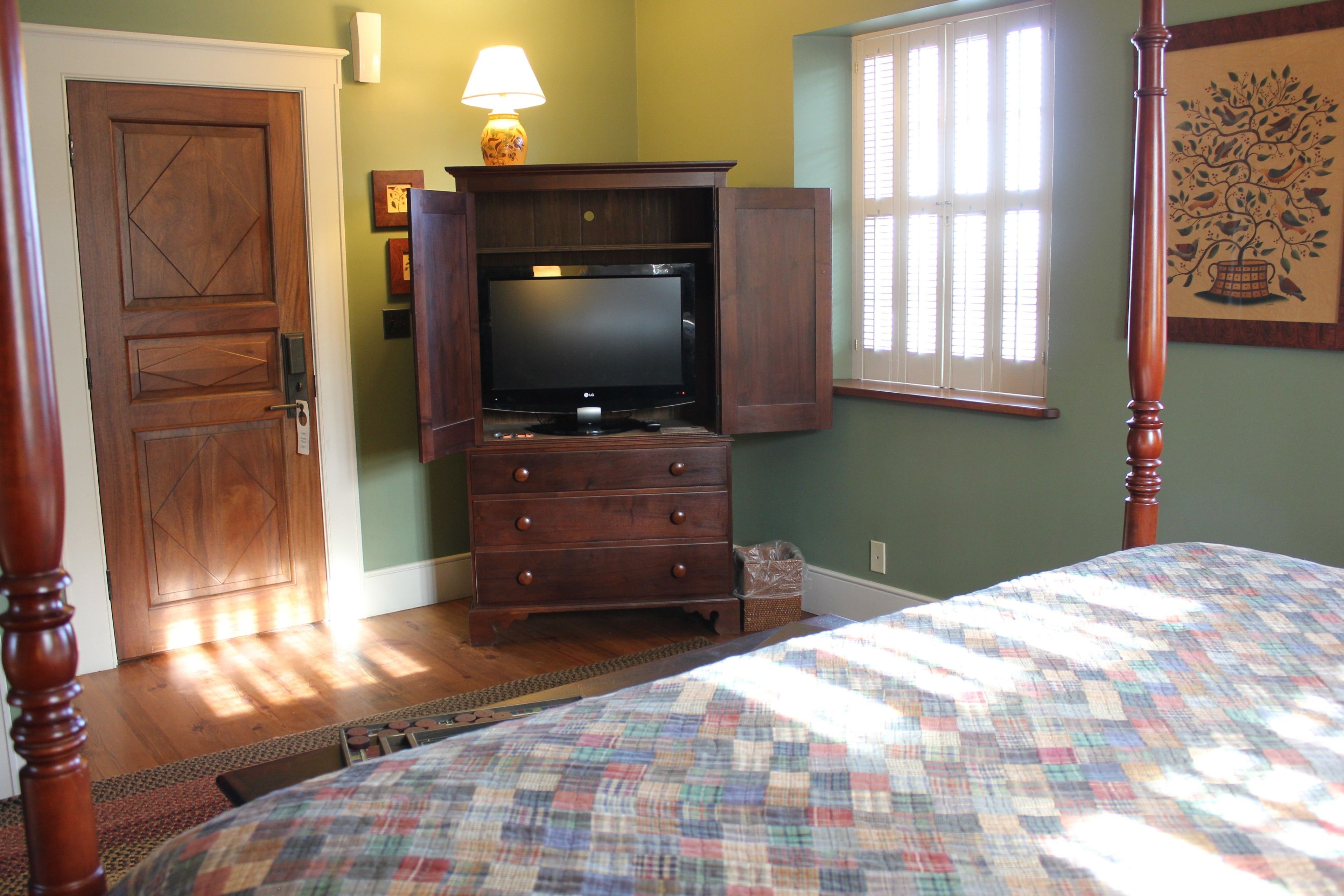 A bedroom with a bed, a dresser with an open cabinet, a television, a lamp, and a window with blinds.
