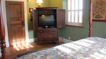 Un dormitorio con una cama, un aparador con un mueble abierto, un televisor, una lámpara y una ventana con persianas.