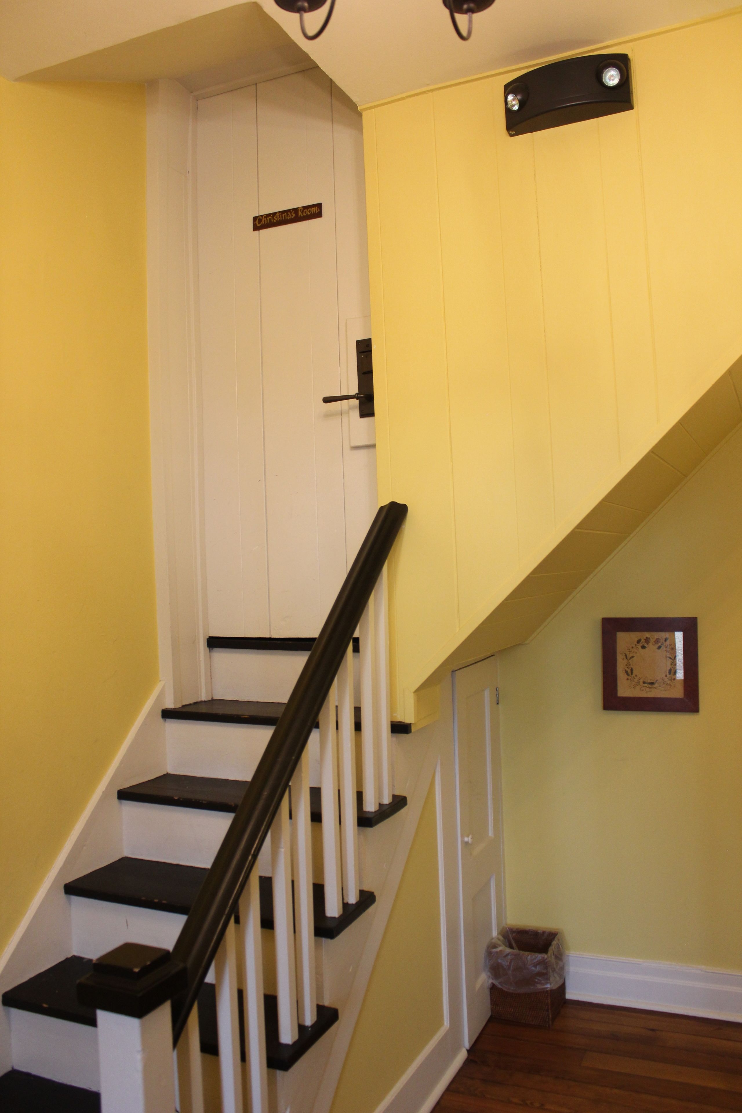 A staircase with black and white railings, a white door with a sign above it, and a small trash bin at the bottom.