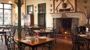A restaurant with multiple tables and chairs, a fireplace, and antler decorations on the walls. - Inn at Hermannhof (Hermann)
