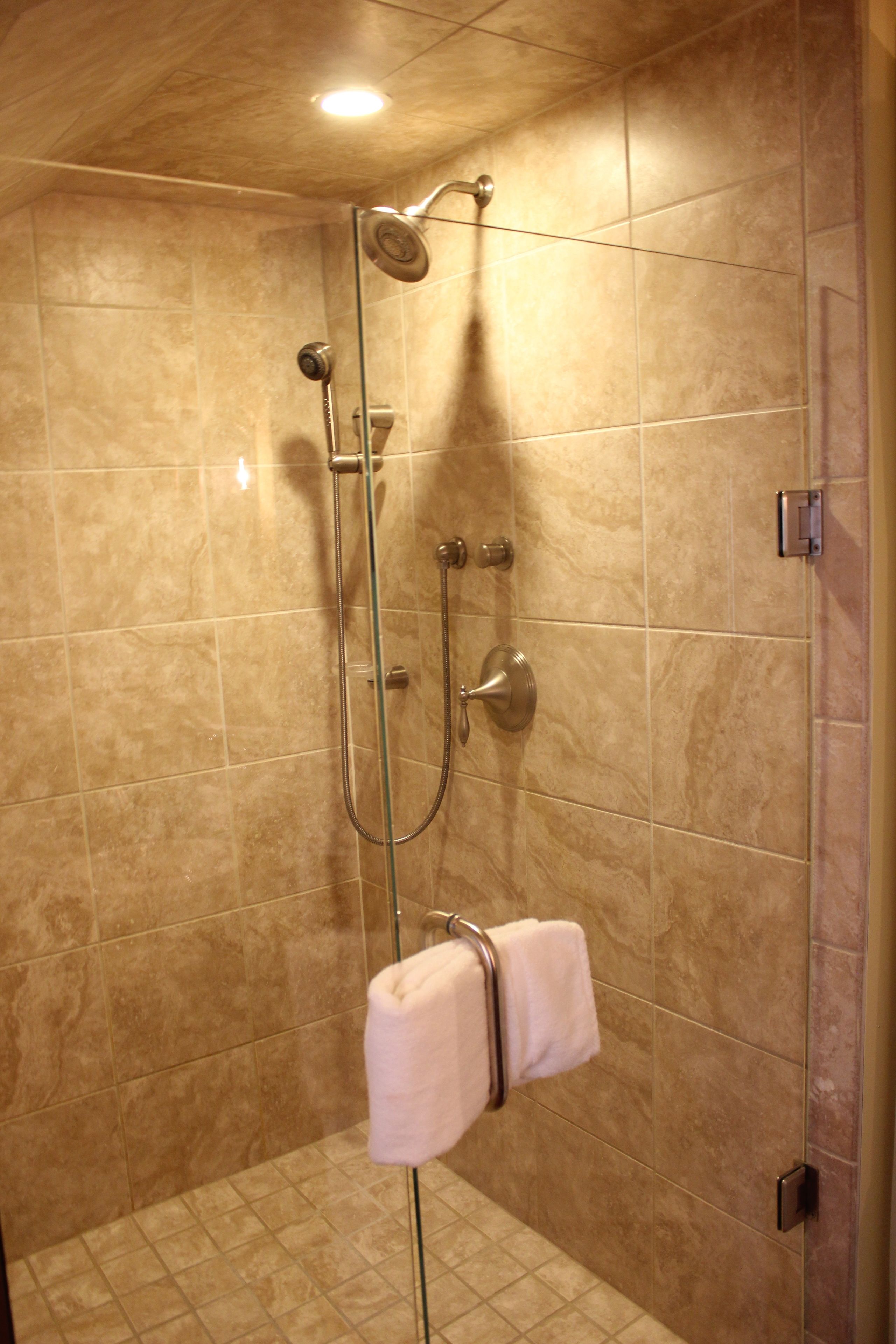 A shower area with beige tiles, a glass door, and a towel hanging on the door handle.
