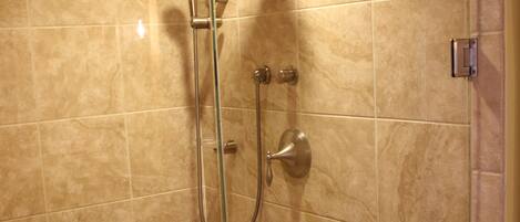 A shower area with beige tiles, a glass door, and a towel hanging on the door handle.