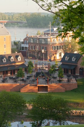 A riverside town with historic buildings, outdoor seating areas, and a bridge in the background.