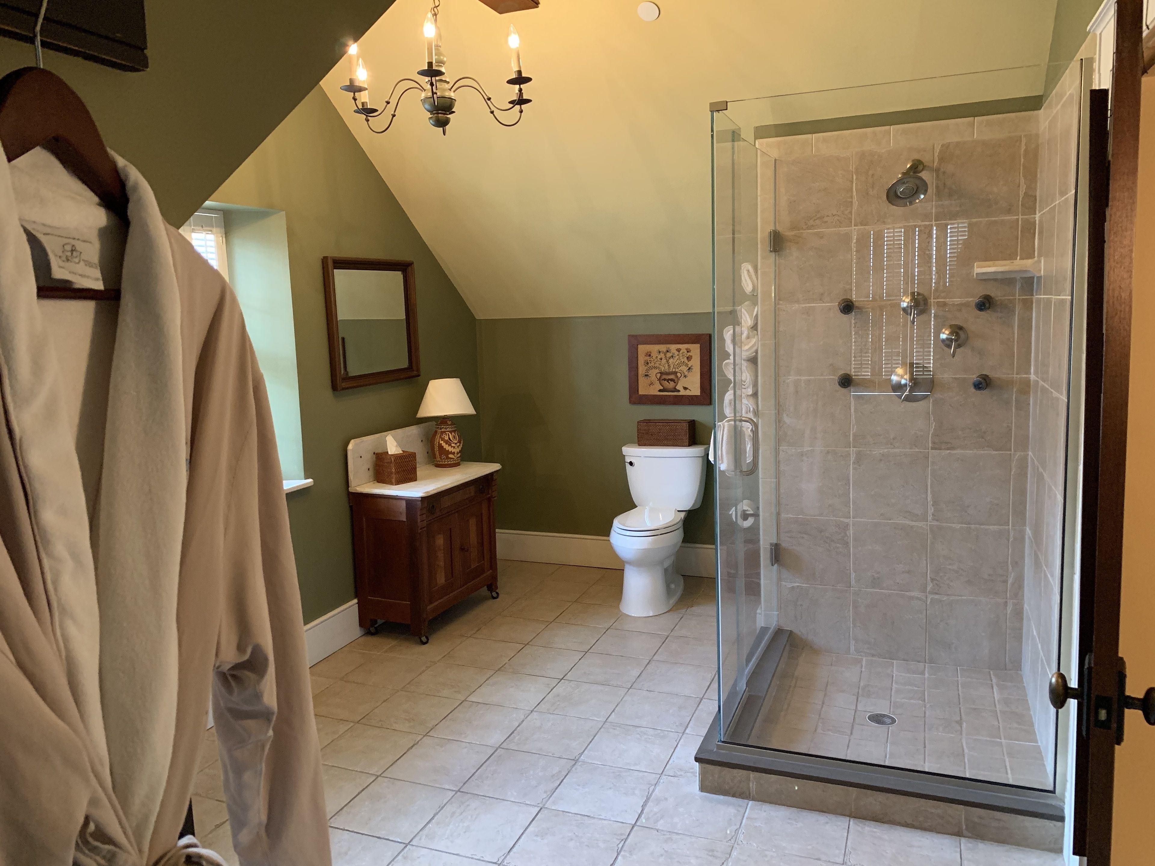 Een badkamer met een glazen douchecabine, toilet, wastafel met spiegel en een kroonluchter.
